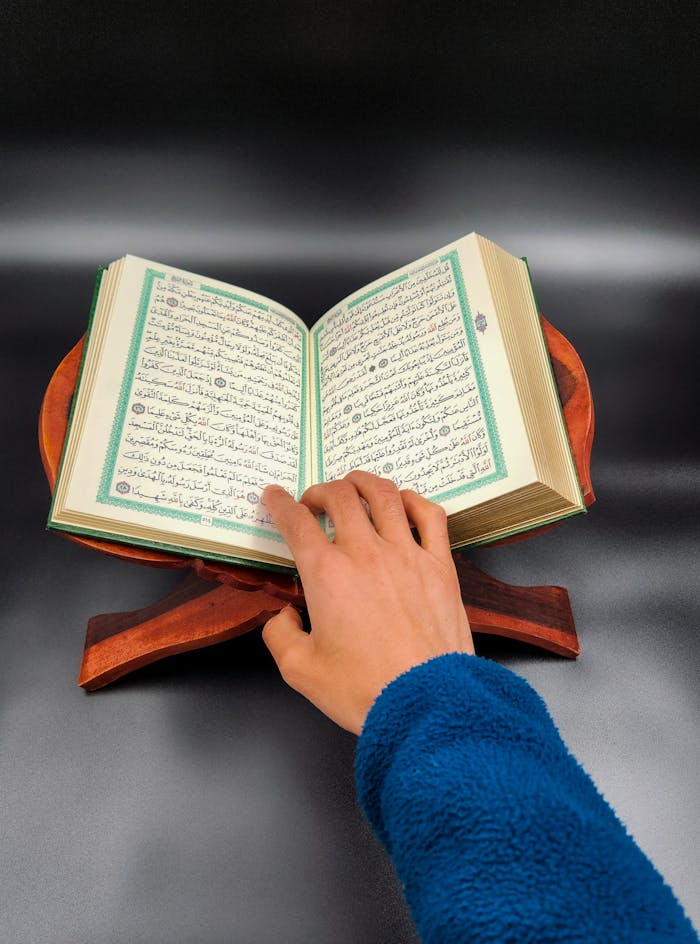 Hand resting on open Quran on a wooden stand, reflecting religious devotion.