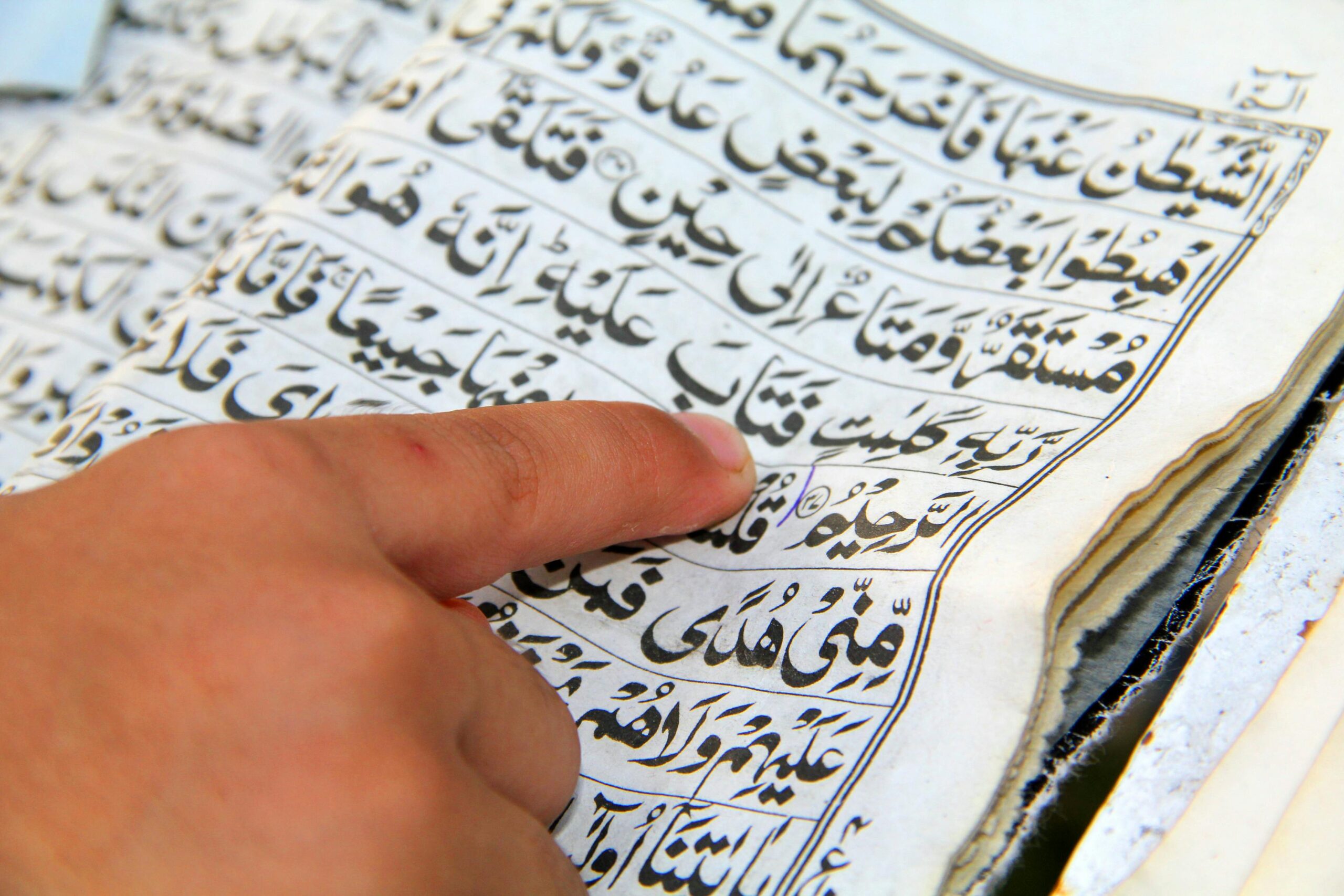 Close-up of a finger pointing to Quranic text, emphasizing study and recitation.